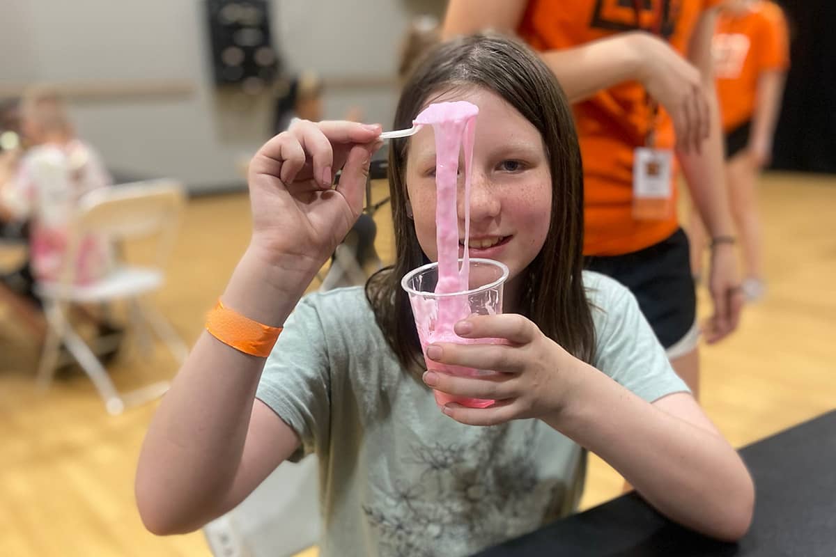 Smiling girl holding pink slime in a cup during an indoor craft activity.