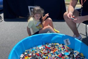 Child playing near a blue tub filled with colorful LEGO bricks at an outdoor activity event.