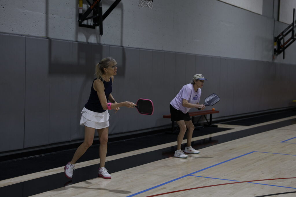 Two women play pickleball in a gym