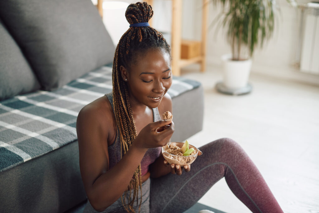 A woman sits in her living room eating a healthy meal before her morning workout.