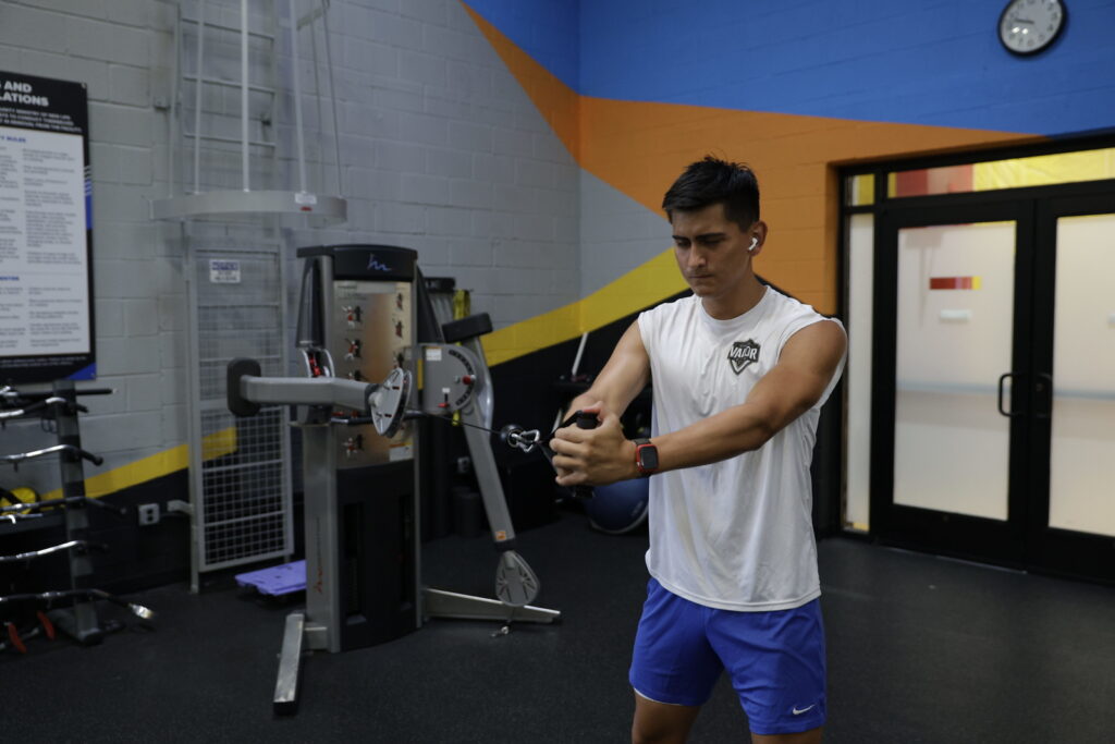 A man in a white muscle t-shirt completes an arm workout at the nZone gym